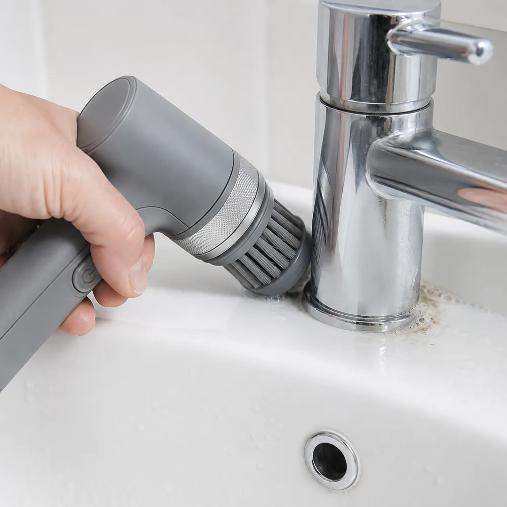 The round brush head reaching into the tight seam around the base of a chrome tap