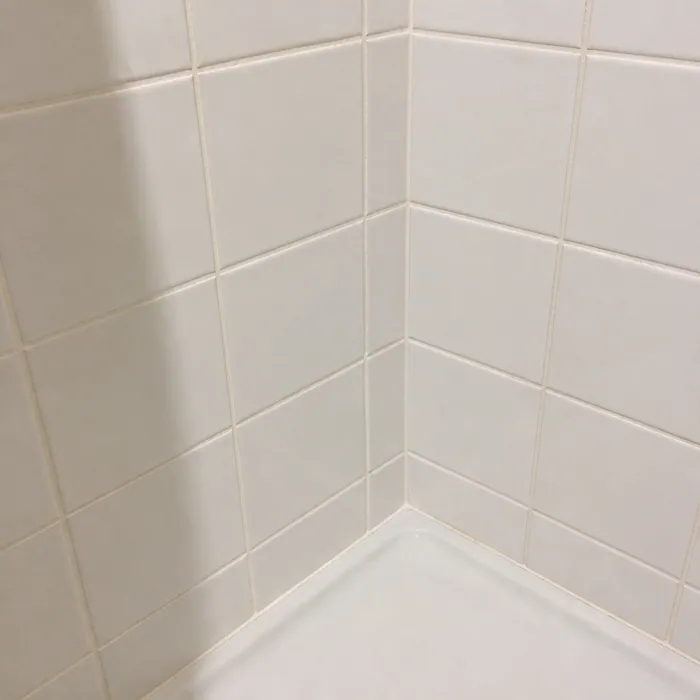 The same shower tile corner with pale clean grout after cleaning
