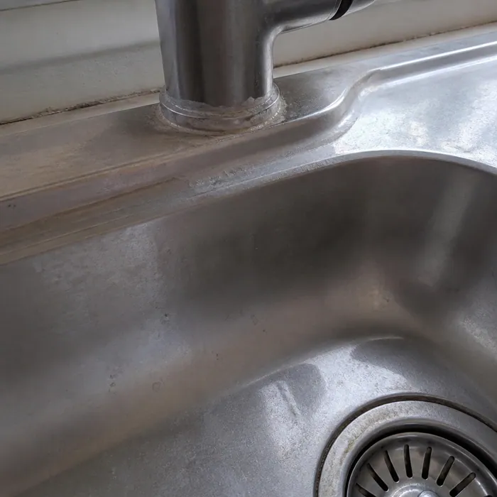 Kitchen sink and tap base with limescale and water-spotted film before cleaning